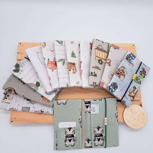 Handgefertigte Mutter-Kind-Pass-Hülle aus biozertifizierter Baumwolle mit E-Card-Fach, Gummiband-Verschluss und dekorativen Holzperlen – nachhaltig, stilvoll und praktisch.