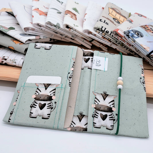 Handgefertigte Mutter-Kind-Pass-Hülle aus biozertifizierter Baumwolle mit E-Card-Fach, Gummiband-Verschluss und dekorativen Holzperlen – nachhaltig, stilvoll und praktisch.