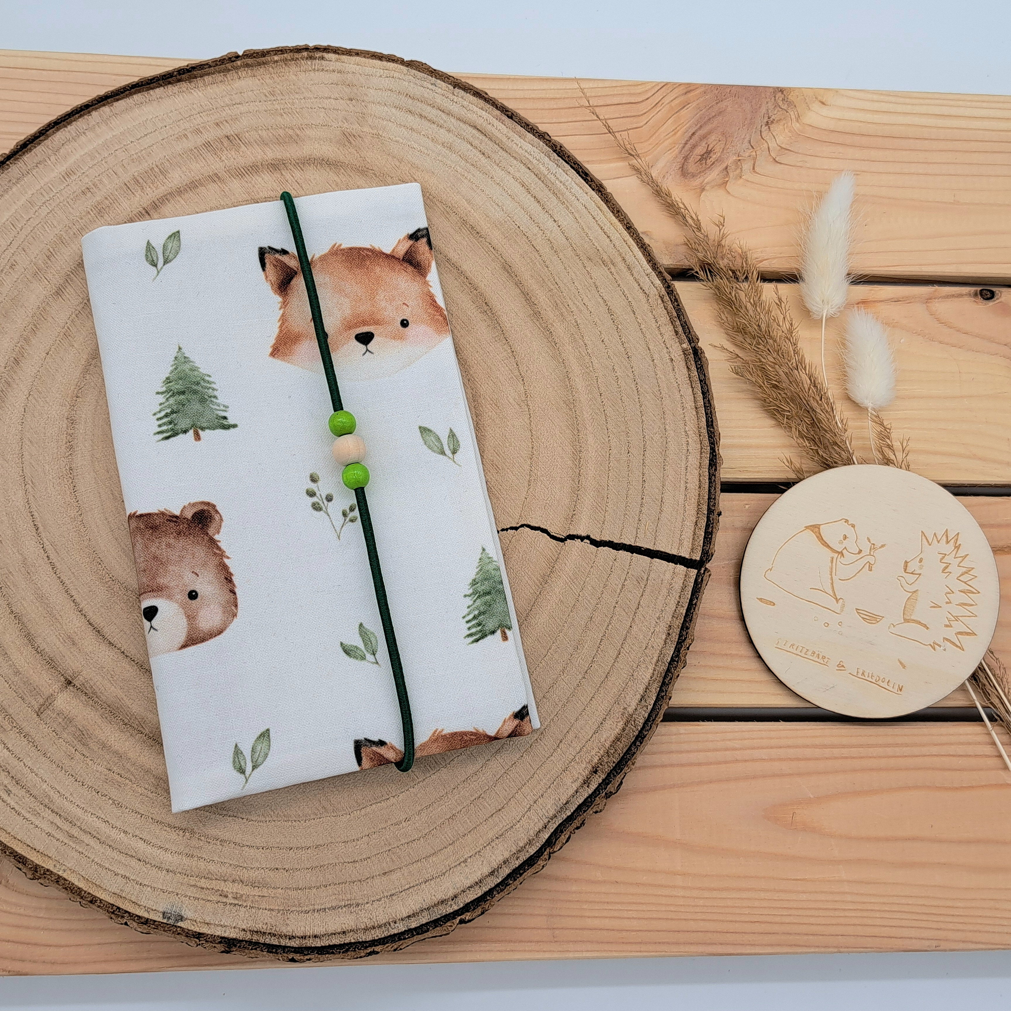 Handgefertigte Mutter-Kind-Pass-Hülle aus biozertifizierter Baumwolle mit E-Card-Fach, Gummiband-Verschluss und dekorativen Holzperlen – nachhaltig, stilvoll und praktisch. Niedliches Design mit Bär, Fuchs, Bäumen und Blätter.