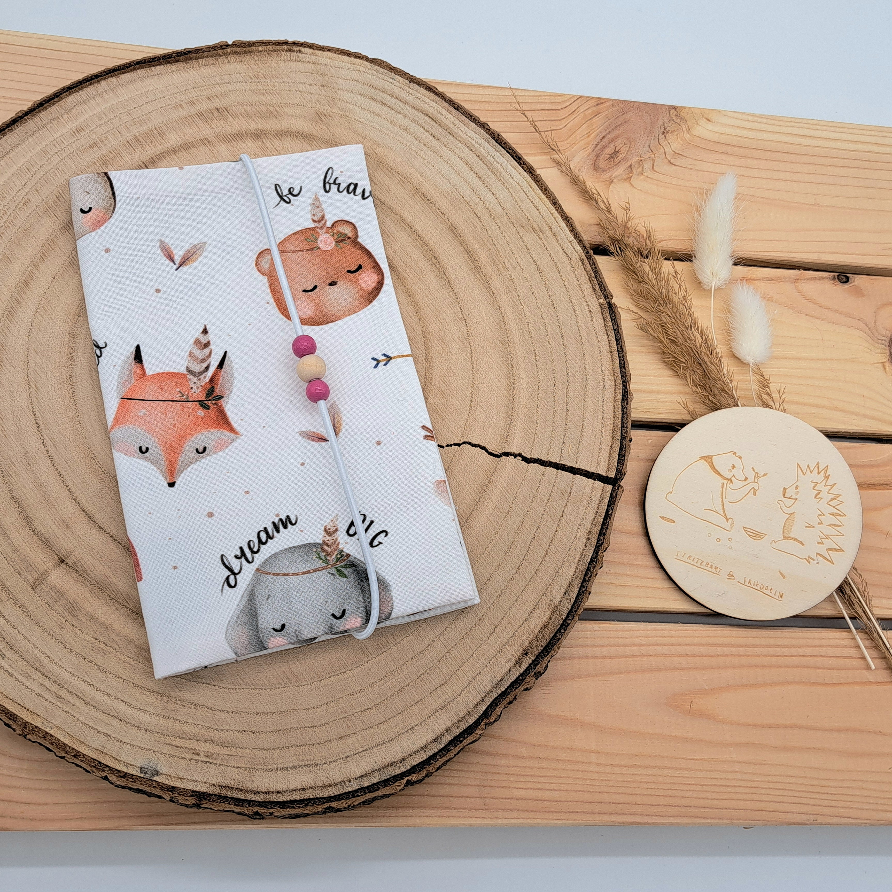 Handgefertigte Mutter-Kind-Pass-Hülle aus biozertifizierter Baumwolle mit E-Card-Fach, Gummiband-Verschluss und dekorativen Holzperlen – nachhaltig, stilvoll und praktisch. Schlichtes und niedliches Design mit Tiere im Indianer-Bohostil. Mit kleinen Sprüchen wie 