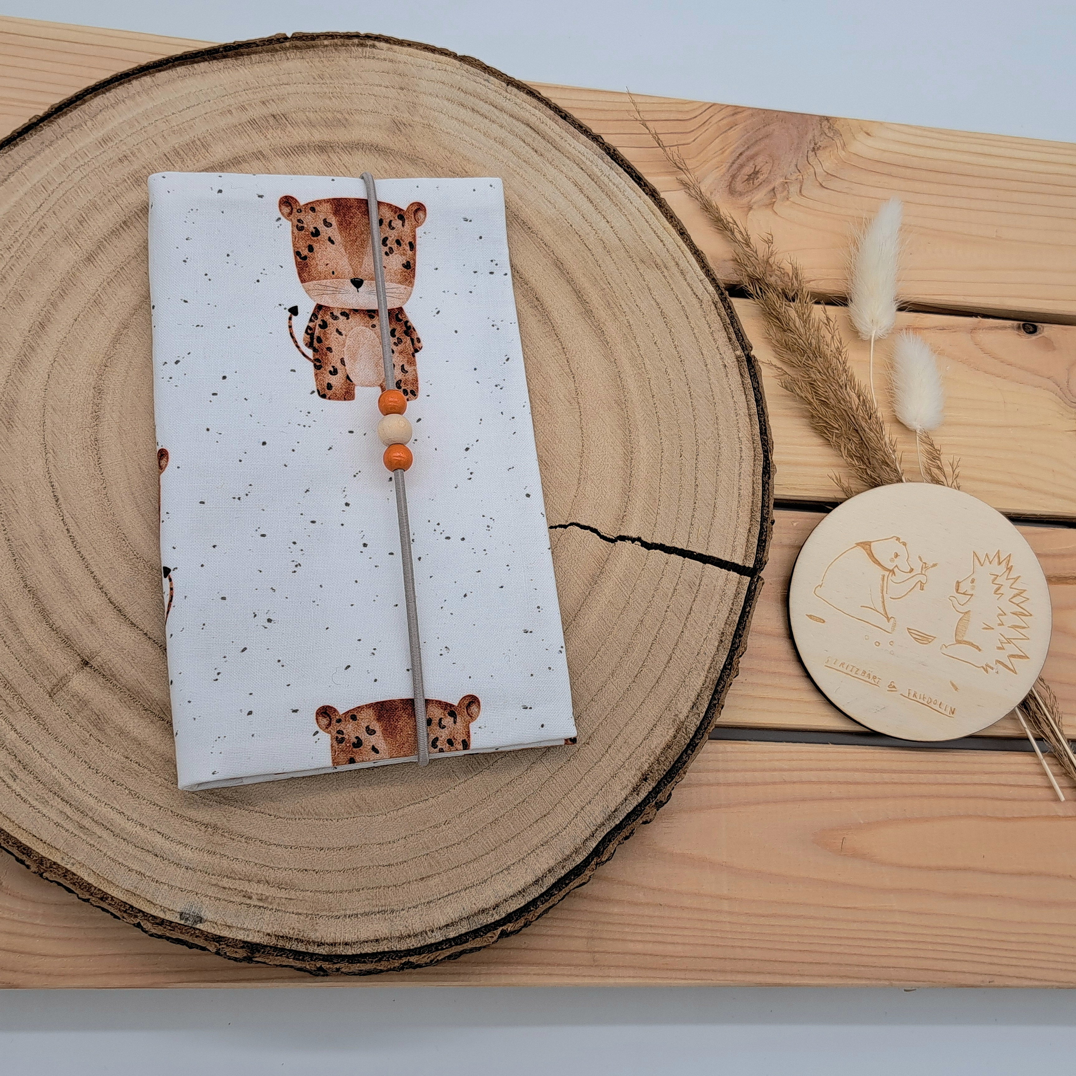 Handgefertigte Mutter-Kind-Pass-Hülle aus biozertifizierter Baumwolle mit E-Card-Fach, Gummiband-Verschluss und dekorativen Holzperlen – nachhaltig, stilvoll und praktisch. Neutrales Design mit zarten Punkten und einen kleinen süßen Leoparden.