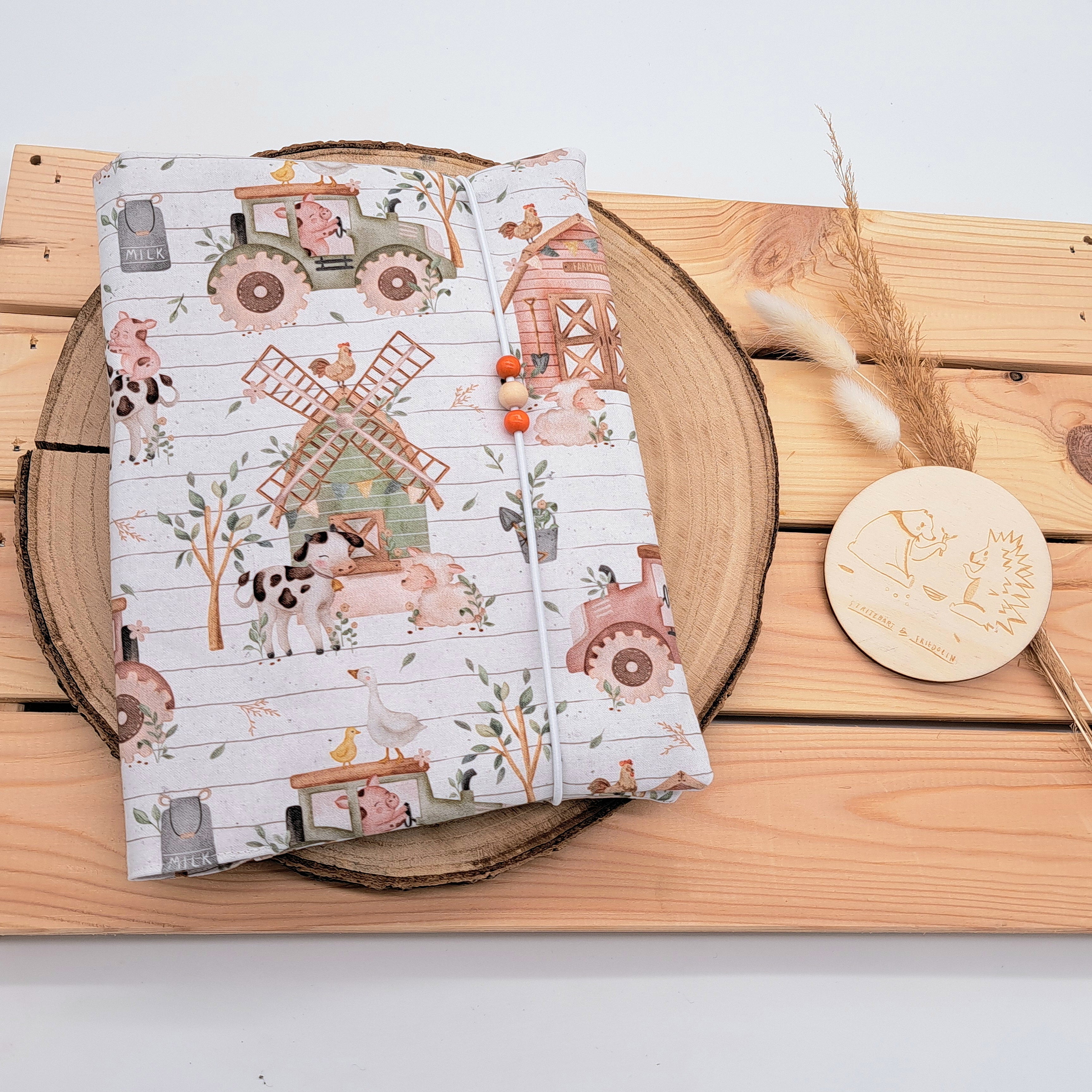 Handgefertigte Windeltasche aus 100% Bio-Baumwolle mit Fach für Windeln und Feuchttücher, Gummikordel-Verschluss mit Holzperlen; nachhaltiges und praktisches Accessoire für Eltern unterwegs. Neutrales Bauernhofmotiv. In dieser Bauernhofwelt sieht man Kühe, Schweine, Kücken, Schafe, Gänse und Traktoren.