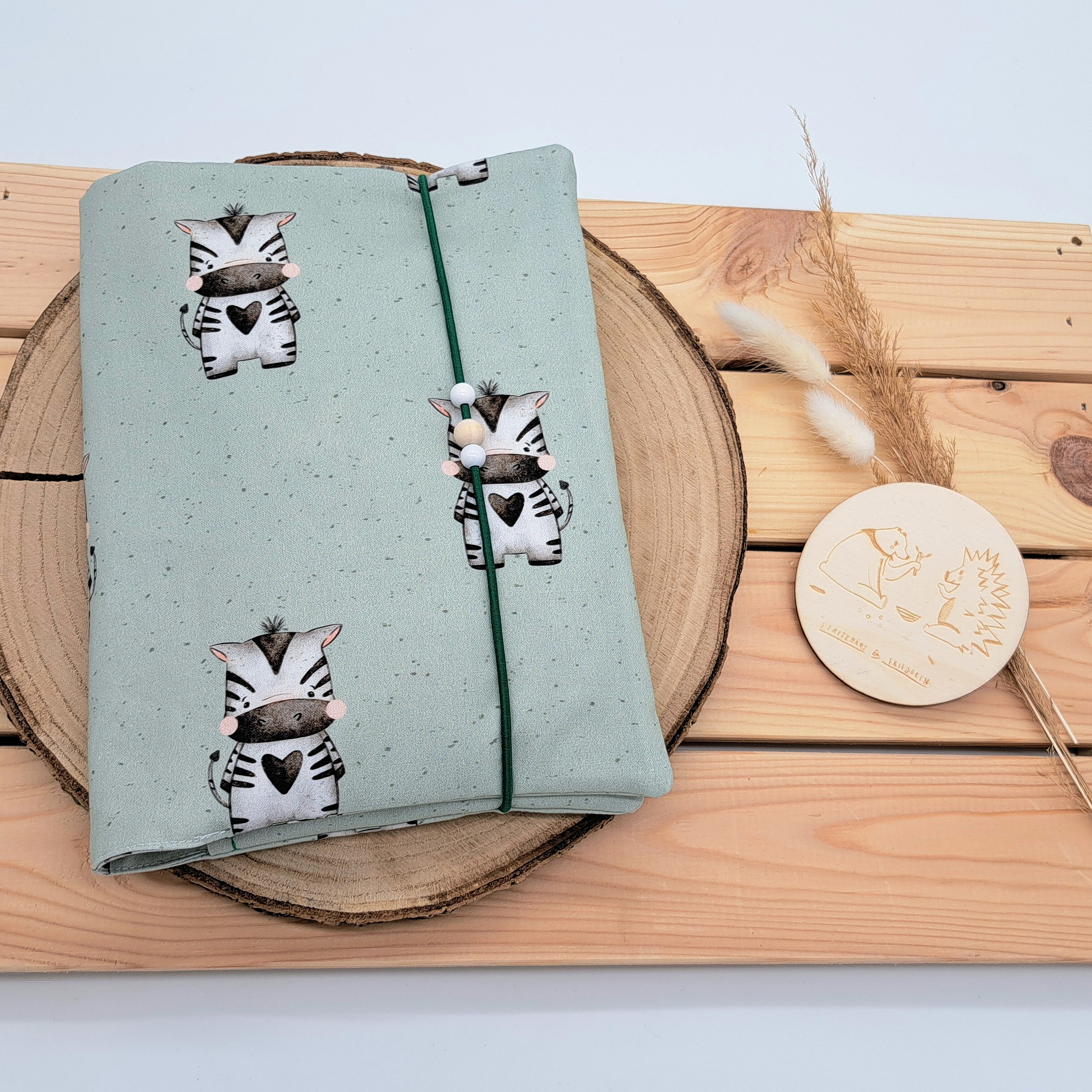 Handgefertigte Windeltasche aus 100% Bio-Baumwolle mit Fach für Windeln und Feuchttücher, Gummikordel-Verschluss mit Holzperlen; nachhaltiges und praktisches Accessoire für Eltern unterwegs. Niedliches und neutrales mintfarbiges Design. Darauf ist ein freundliches Zebra zu sehen.