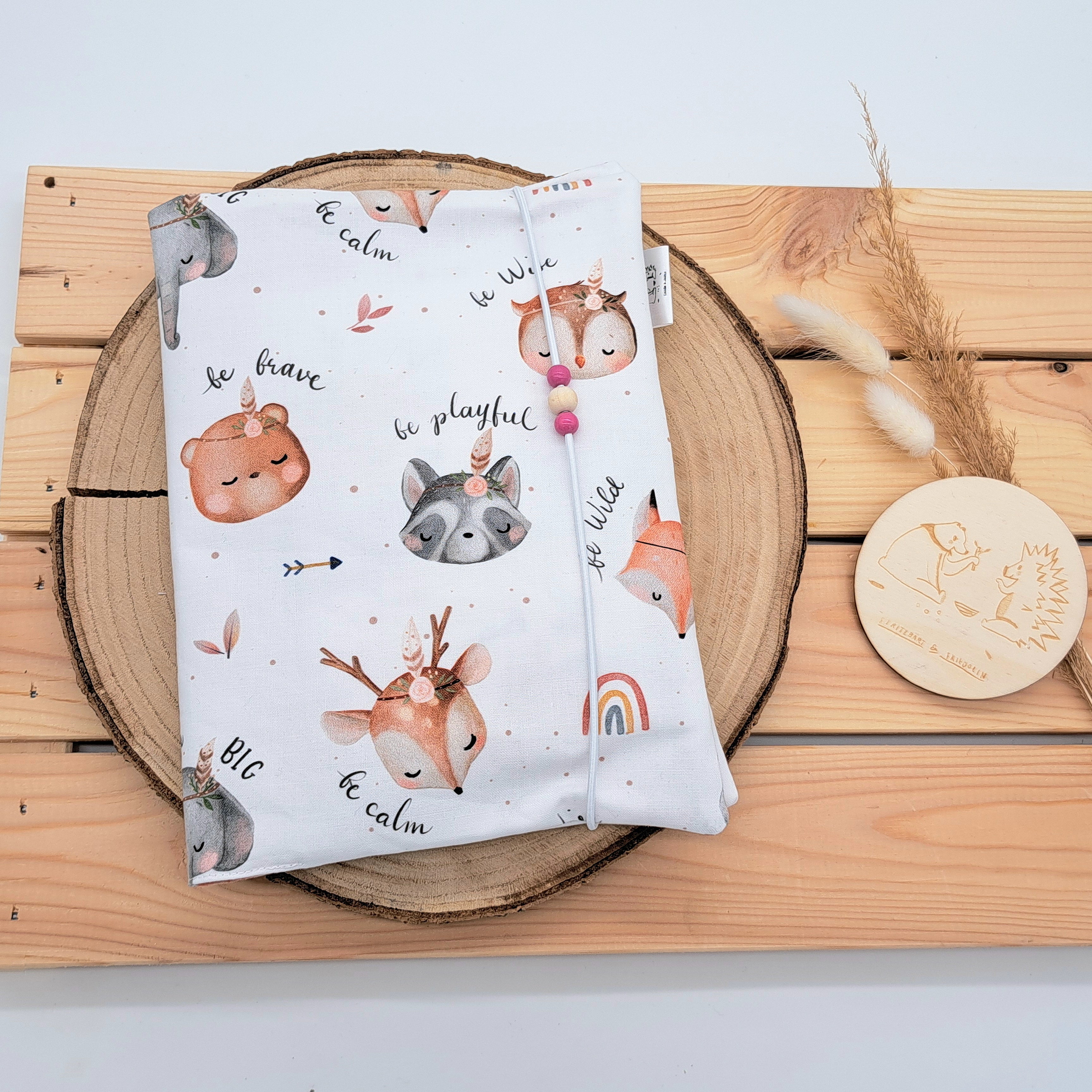 Handgefertigte Windeltasche aus 100% Bio-Baumwolle mit Fach für Windeln und Feuchttücher, Gummikordel-Verschluss mit Holzperlen; nachhaltiges und praktisches Accessoire für Eltern unterwegs. Niedliches Mädchendesign. Schlicht und im bohostil gehalten. Darauf sind Tiere mit Indianerfedern und Sprüchen wie 