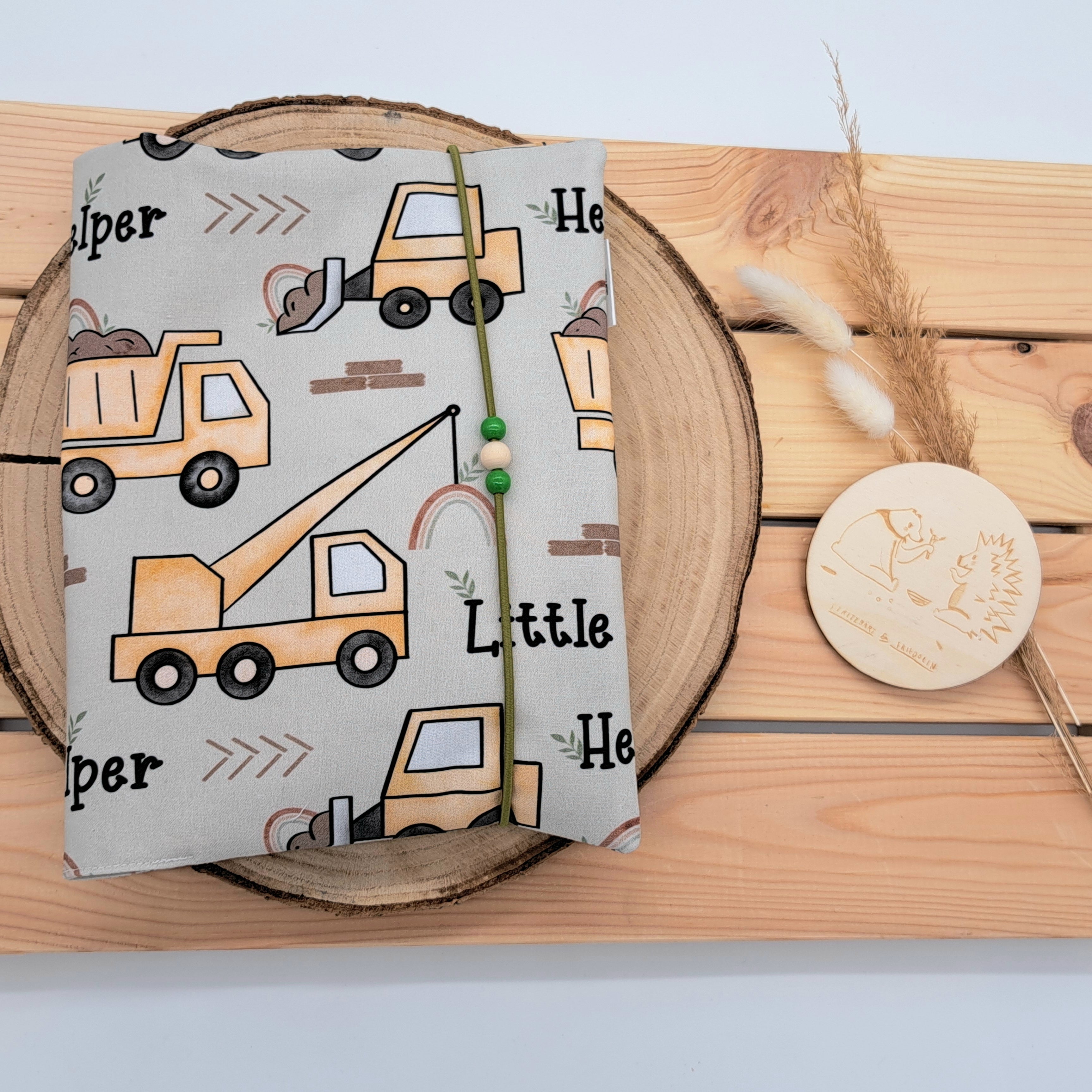 Handgefertigte Windeltasche aus 100% Bio-Baumwolle mit Fach für Windeln und Feuchttücher, Gummikordel-Verschluss mit Holzperlen; nachhaltiges und praktisches Accessoire für Eltern unterwegs. Schlichtes Design im Baustellenstil mit Ockerfarbenen Fahrzeugen und der Aufschrift 